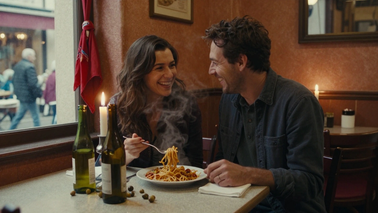 Two people laughing over pasta in a warm, candlelit trattoria with wine bottles and olive pits on the table.