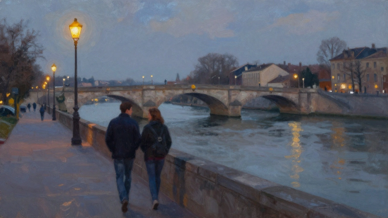 Two people walking by a river near a historic bridge at dusk.